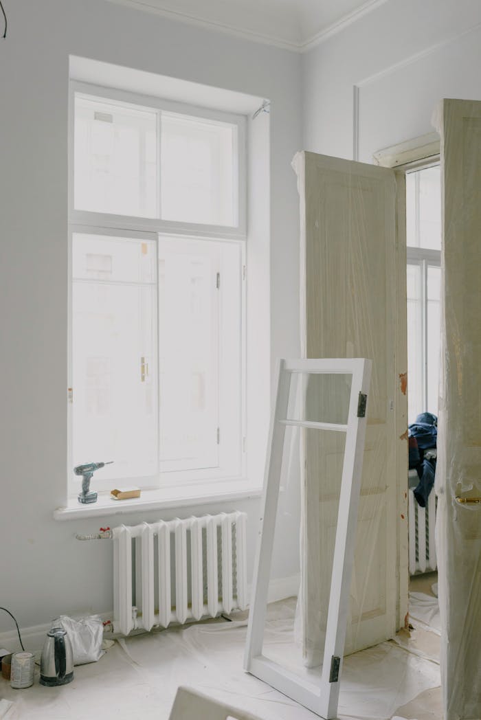 Window frame on floor near wooden doors and heating system in light apartment during renovation process